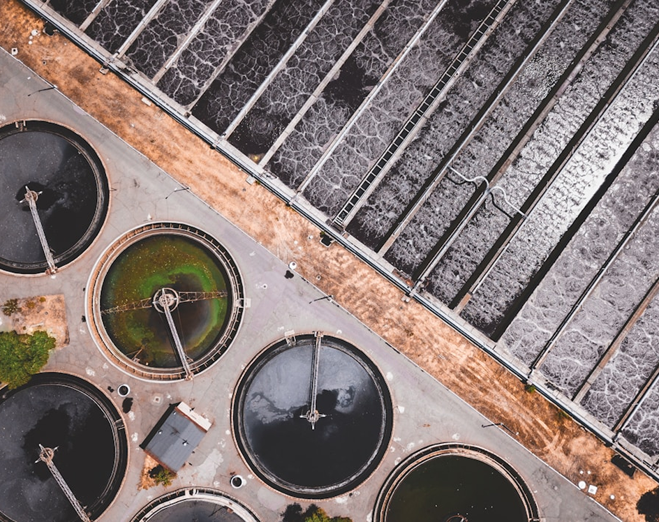 Aerial view of circular and rectangular tanks at a wastewater treatment plant with aeration lines and walkways.